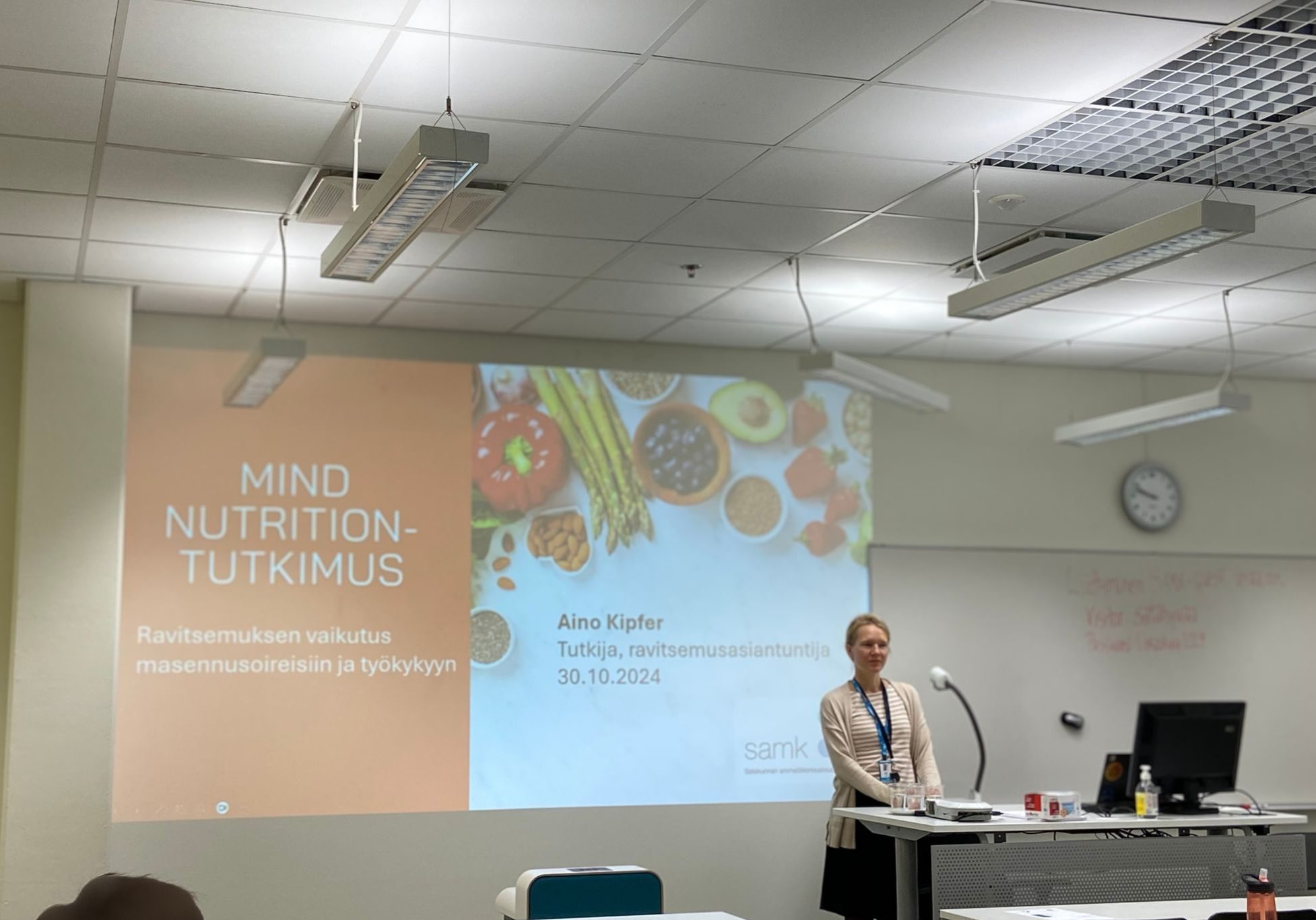 Aino Kipfer seisoo ison näytön edessä, kertomassa Mind Nutrition -tutkimuksesta. 